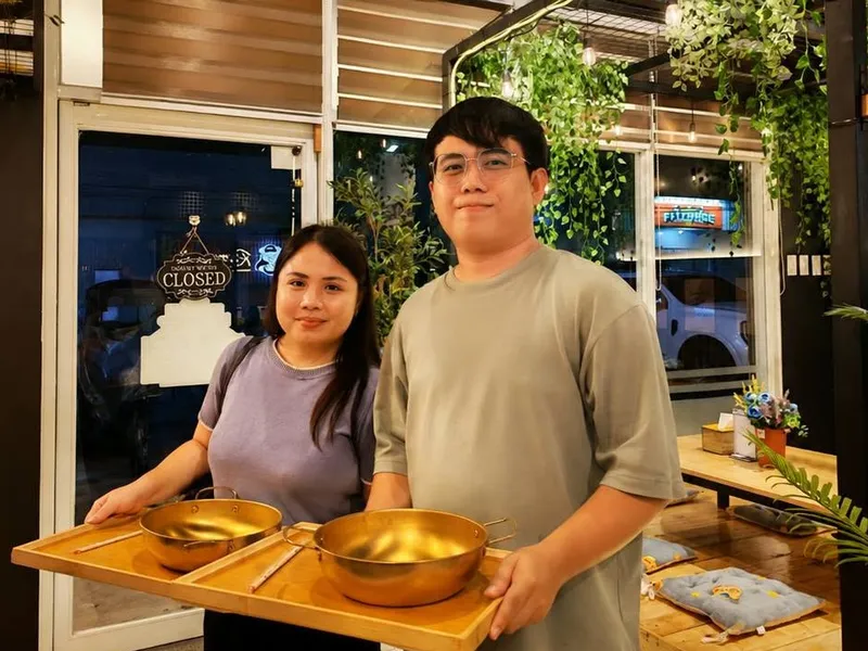 Two customers carrying trays of gold hotpots at the K-Stop entrance