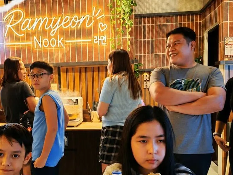 Customers at the cooking stations under the Ramyeon Nook neon sign