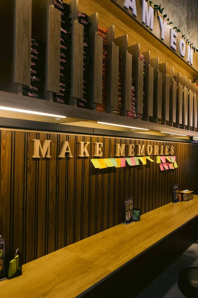 Wall of Korean ramyeon packs above a counter spelling MAKE MEMORIES